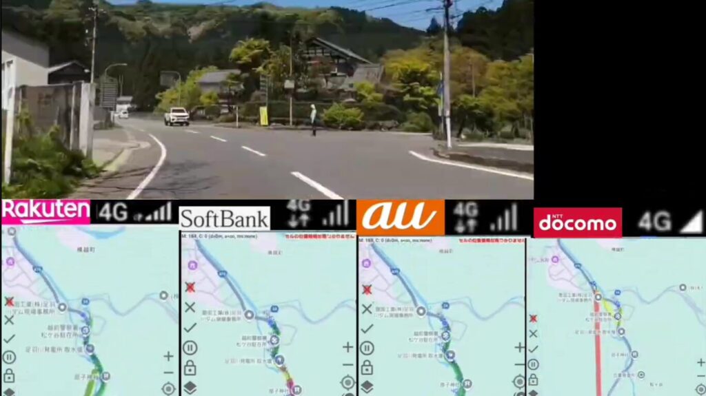 山あいの県道分岐を走行中の車載映像を背景に、画面下部にRakuten 4G・SoftBank 4G+・au 4G・docomo 4Gの電波アイコンを横並びで配置。Rakuten・SoftBank・auはフルバーで良好な電波を示す一方、docomoはアンテナなしで圏外気味。各アイコンの下には、それぞれの走行ルートと電波強度を色分け表示した地図スクリーンショットが4枚並び、山間部でのキャリア別通信状況を視覚的に比較できる構成。
