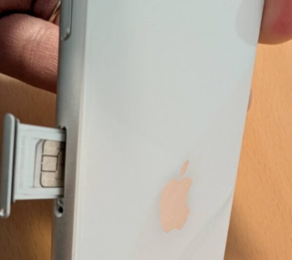iPhoneのSIMスロットからトレイを引き出しnanoSIMカードを挿入する手元のクローズアップ写真
