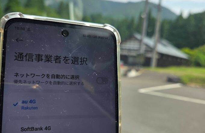 福井県池田町かずら橋駐車場で撮影した写真、スマホ画面の通信事業者選択には「au 4G(Rakuten)」と表示され、楽天モバイルは自社回線ではなくパートナー回線のauに接続されていることが分かる様子