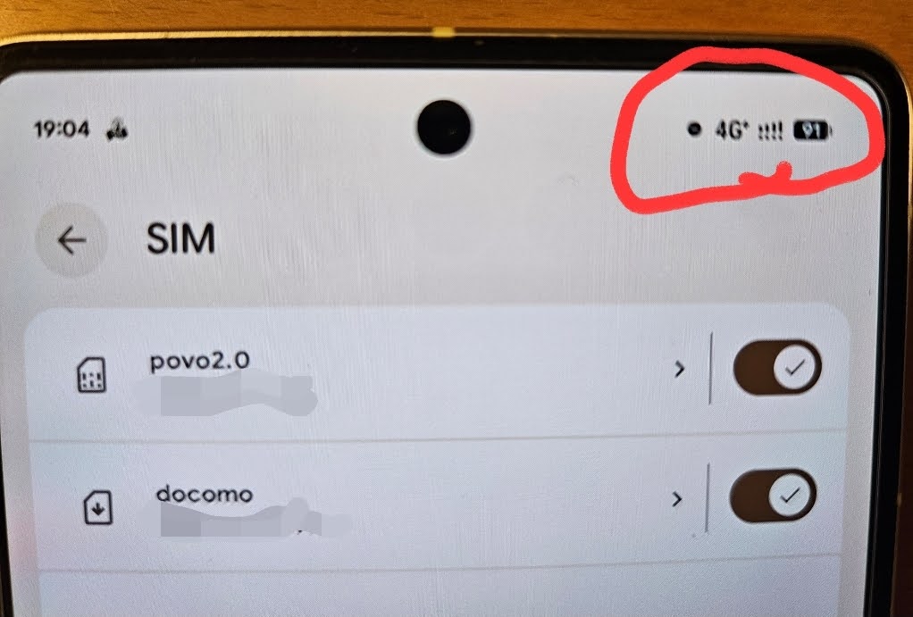 スマートフォンのSIM設定画面の実物写真。上部のステータスバーには4G+の電波がフルスロットで立っていることが赤枠で強調されている。設定項目には「povo2.0」と「docomo」の2つのSIMカードが有効(オン)になっており、デュアルSIM運用でどちらの回線も安定して受信できている様子を示している。