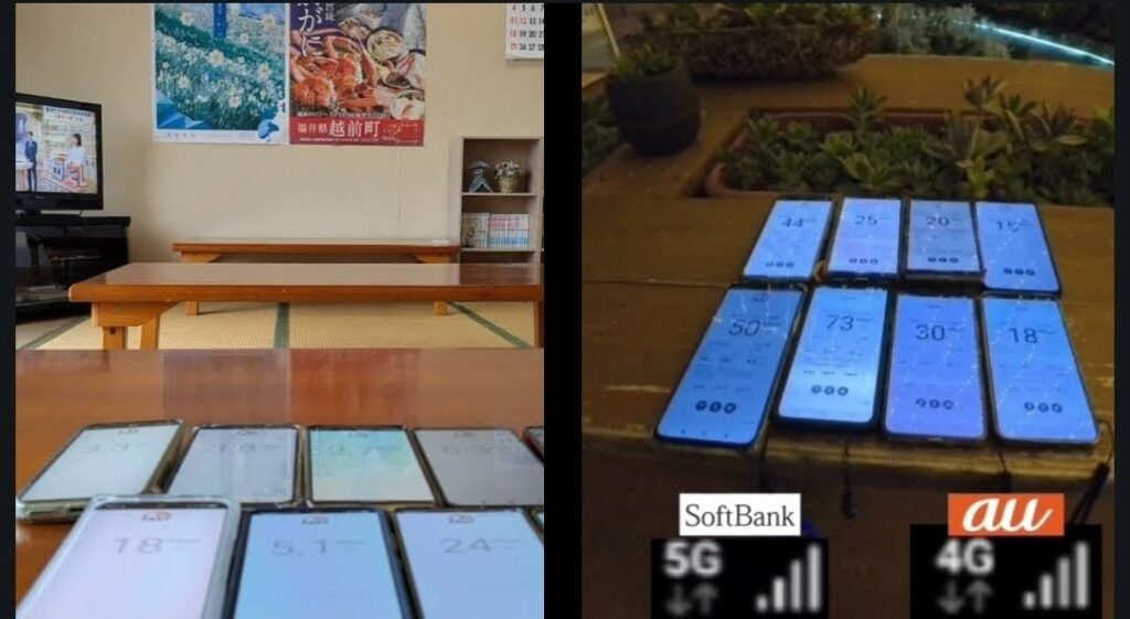 9台のスマートフォンを並べて一斉に計測した通信速度の実測比較画像。手前のテーブルの上に各端末が配置されており、画面には「FAST.com」による計測結果が表示されています。
壁面には「福井県 越前町」のポスターやカレンダー、禁煙マーク、テレビが設置されており、屋内かつ平穏な環境下でのリアルな多端末同時計測データであることが示されています。
