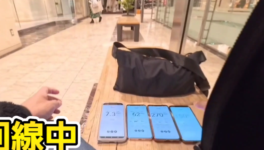 商業施設のベンチに4台のスマートフォンを並べ、通信速度を実測している様子。左から1台目は下り7.3Mbps、2台目は下り62Mbps、3台目は下り270Mbps、4台目は下り150Mbpsを記録しており、端末や回線によって速度差が出ていることがわかる検証画像。
