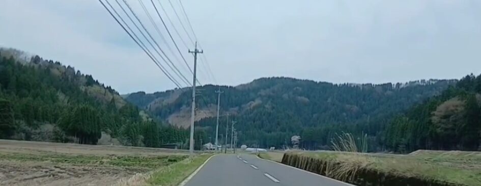 アップロードいただいた画像は、通信速度の数値データではなく**「田舎の風景（山あいの道路）」**のようです。もしこちらの画像に対する代替テキストが必要であれば、以下をご利用ください。

---

山々に囲まれたのどかな田舎道を走る車窓からの風景。道路の左側には電柱が並び、周囲には茶褐色の田畑と深い緑の杉林が広がっている、曇り空の下の静かな景観。

---

**※通信速度の測定結果（数値データ）の画像は、この後お送りいただけるということで相違ないでしょうか？** 数値データの画像が届きましたら、**「下り（ダウンロード）」「上り（アップロード）」「Ping値」**などの詳細な数値をすべて網羅し、一次情報としての価値が伝わる代替テキストを作成いたします。画像をお待ちしております。
