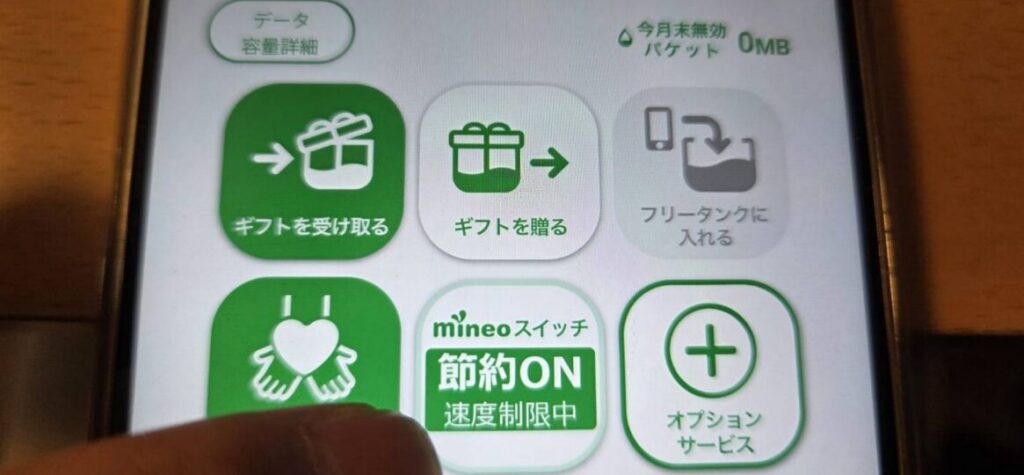 mineoアプリの操作画面。「mineoスイッチ」が緑色の「節約ON(速度制限中)」状態になっている様子。画面右上にはデータ残量に関する「今月末無効パケット 0MB」という数値が表示されている。通信速度を意図的に制限してギガ消費を抑える機能の実機画面。